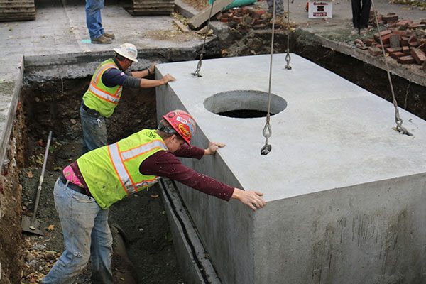 Construction workers in hard hats guide cement block into place